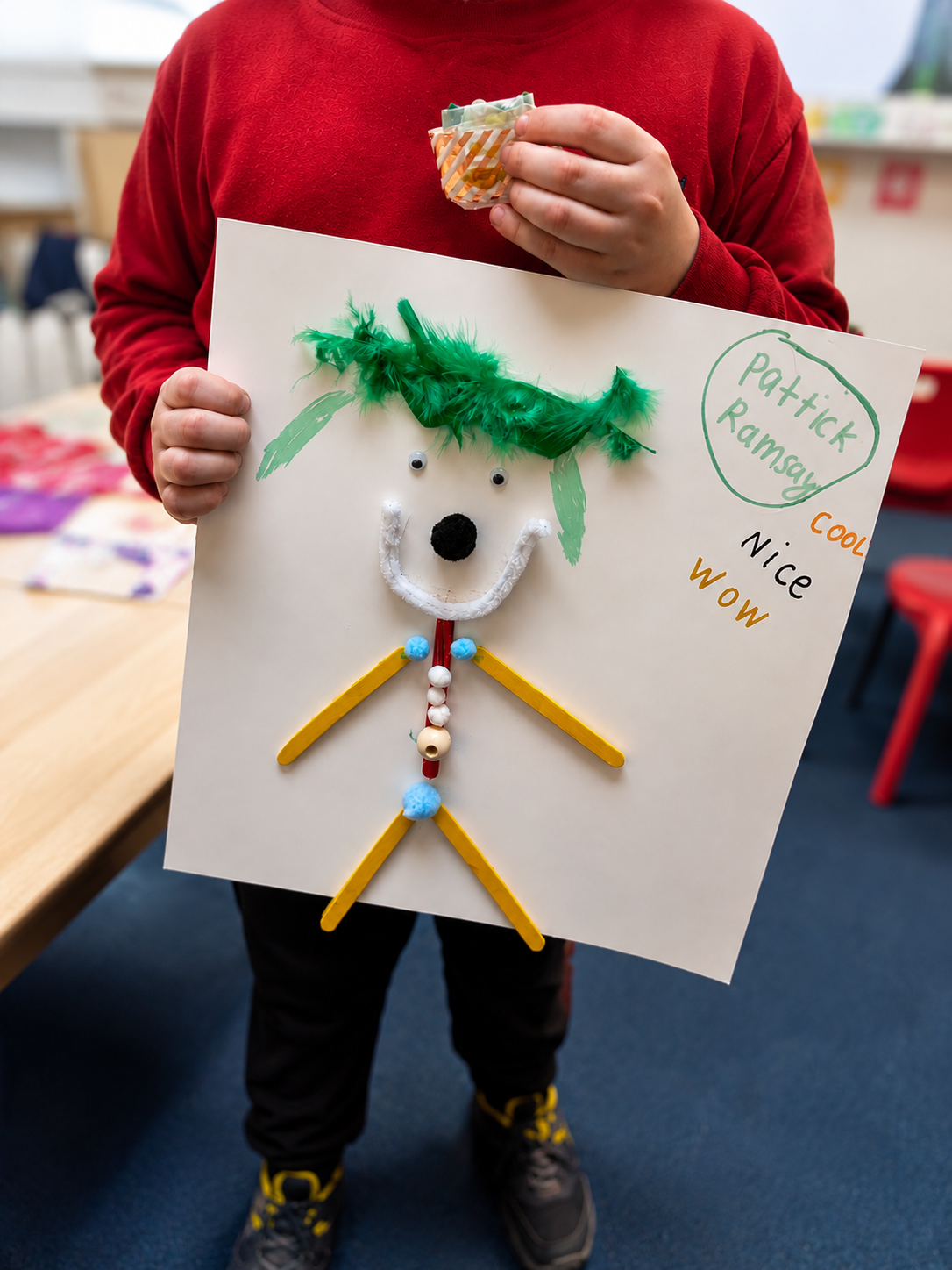 Kid holding a character collage made of sticks and yarn